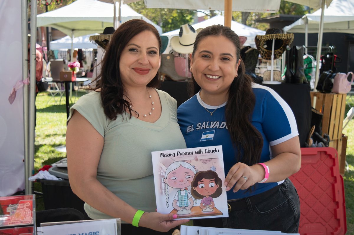 Denise and a reader holding Making Pupusas with Abuela at a Salvadoran cultural event